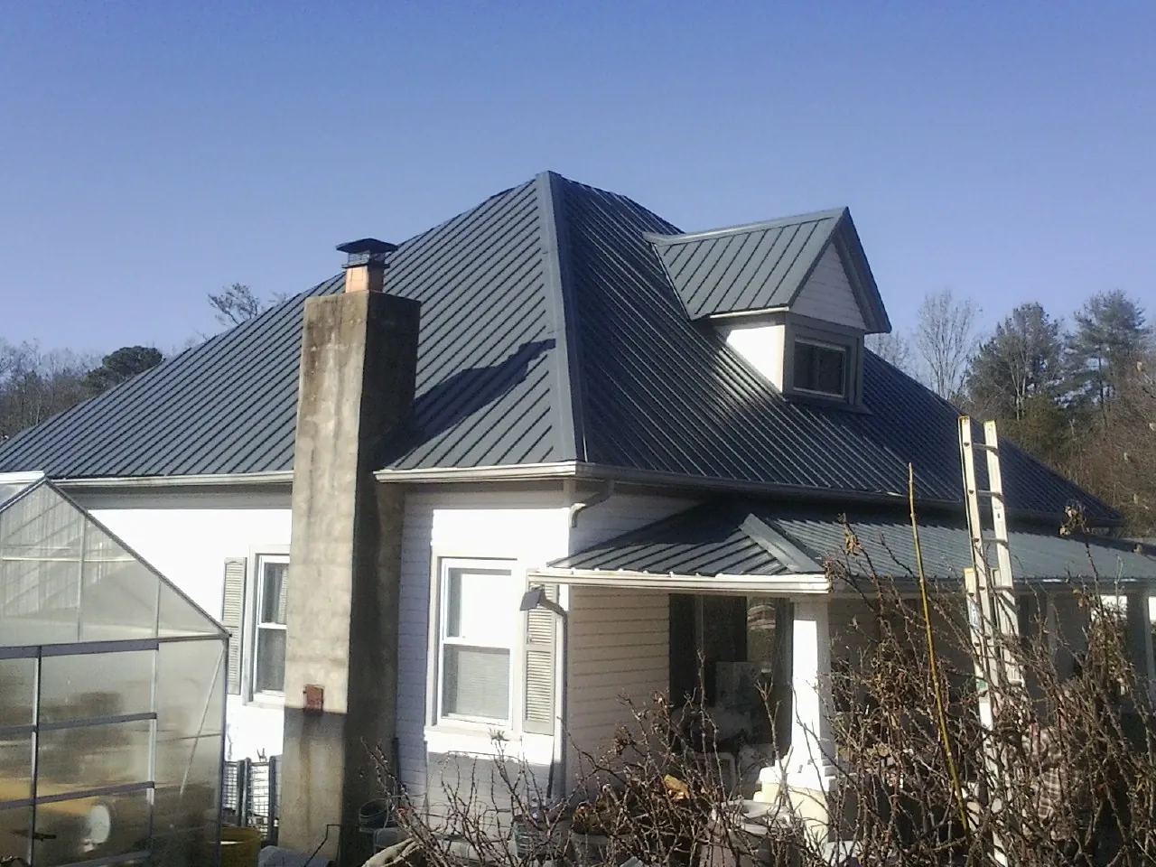 Dark blue standing seam metal roof on a white farmhouse with dormer — Slate & Tile Roof Repair by Roofing Brothers in Odessa