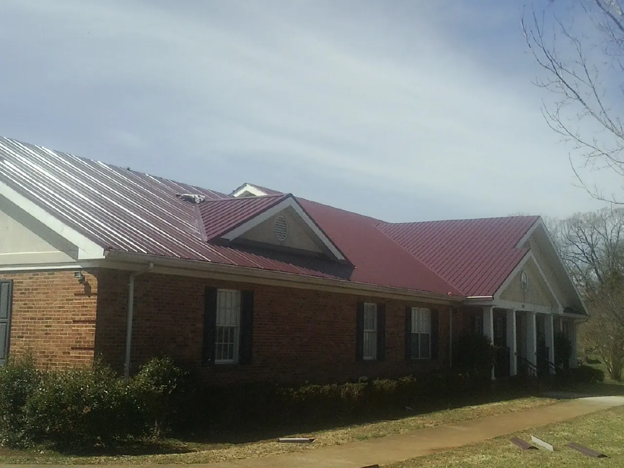 Red metal roof with gabled entries on a long brick building, from a Hail Damage Roof Repair job in Odessa